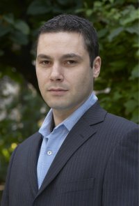 A man with short dark hair wearing a suit jacket and blue shirt