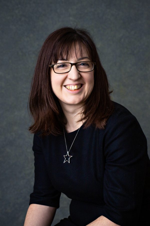 A woman with long dark hair and a dark top smiling into the camera