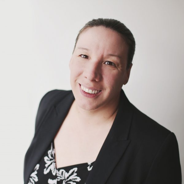 a headshot of a woman wearing a black jacket and black and white top. She is smiling.