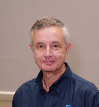 A man with grey hair smiling. He is wearing a blue polo shirt.
