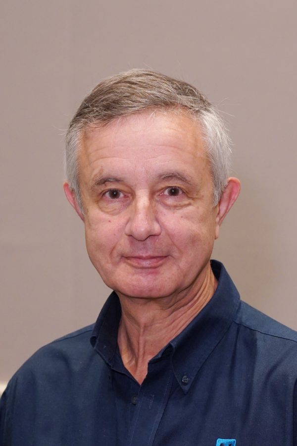 A man with grey hair smiling. He is wearing a blue polo shirt.