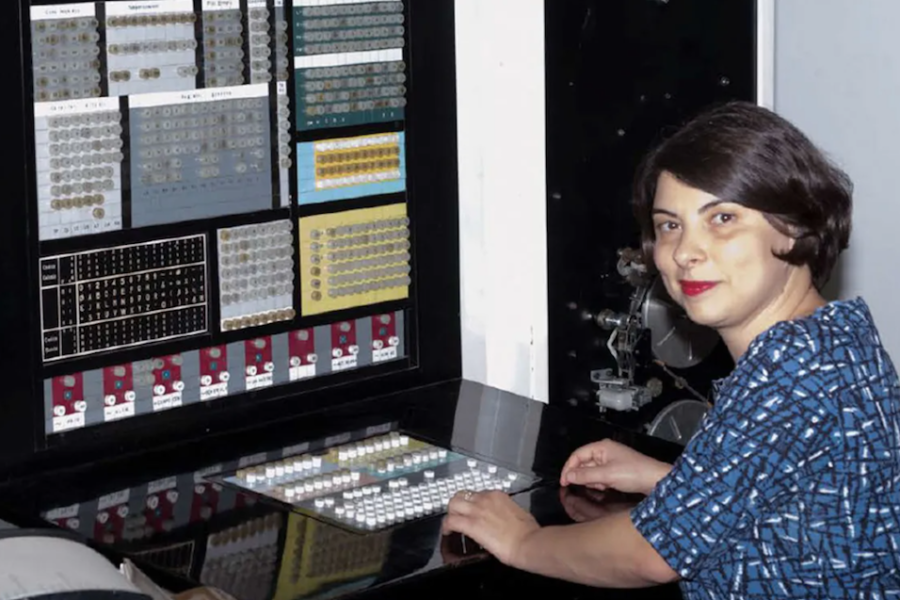 A woman in a blue top sat in front of an old large computer