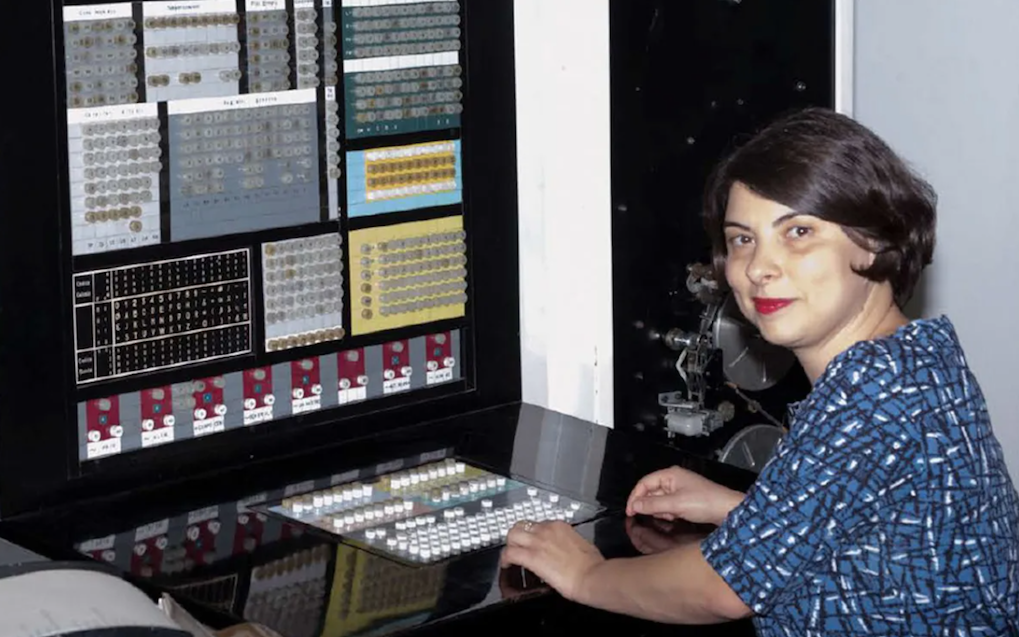 A woman in a blue top sat in front of an old large computer