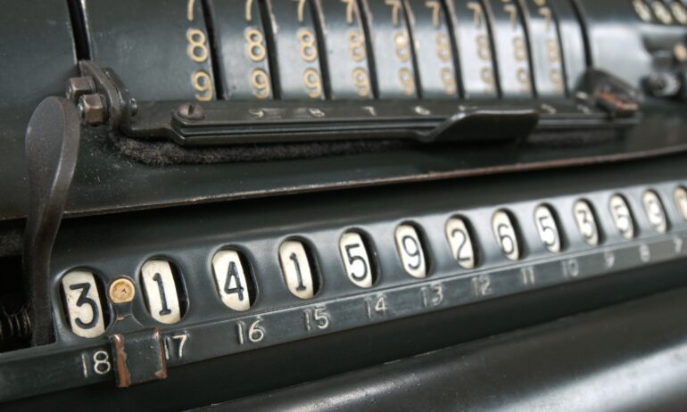 Close up to a vintage calculator with large levers and a number display showing pi