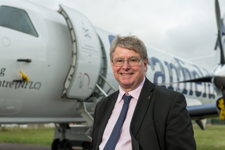 A photograph of Professor Sir Iain Gray standing in front of an airplane