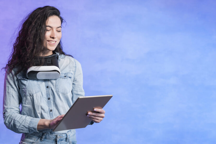 A woman holding a tablet with VR goggles around her neck.